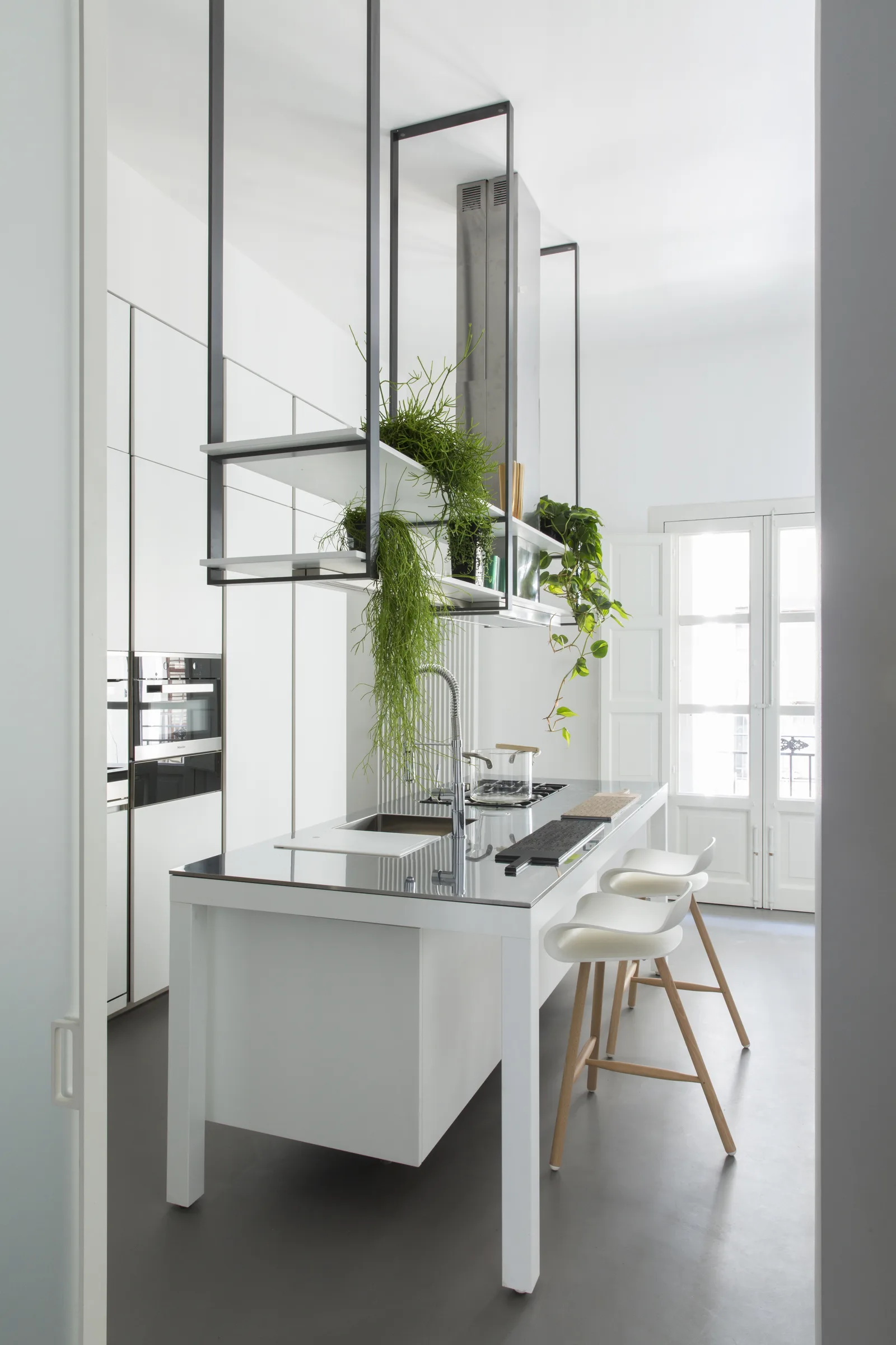 Kitchen island with a suspended metal frame, plants and stools, vertical view