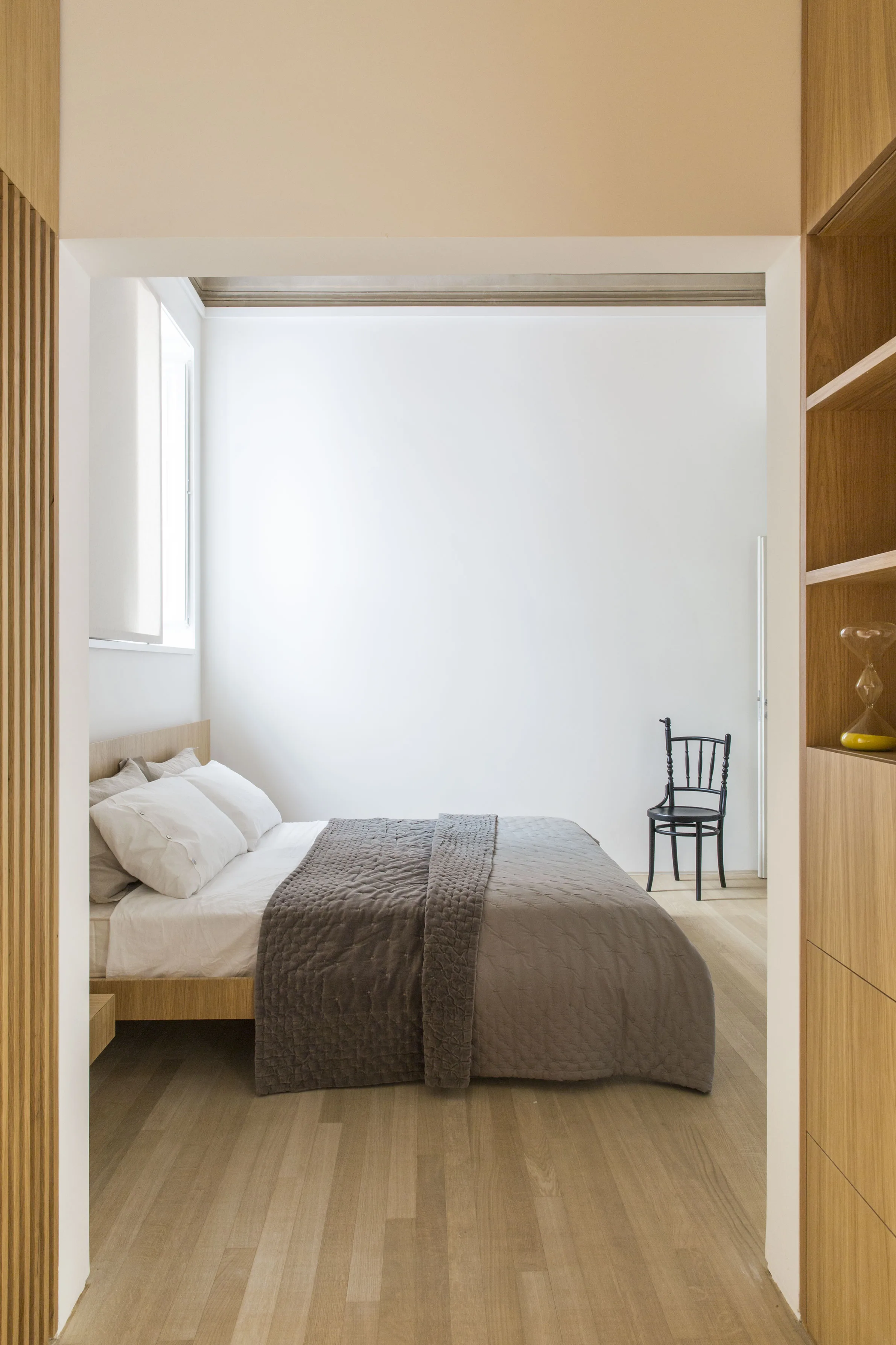 Bedroom with pale parquet and an oak headboard, seen through an opening