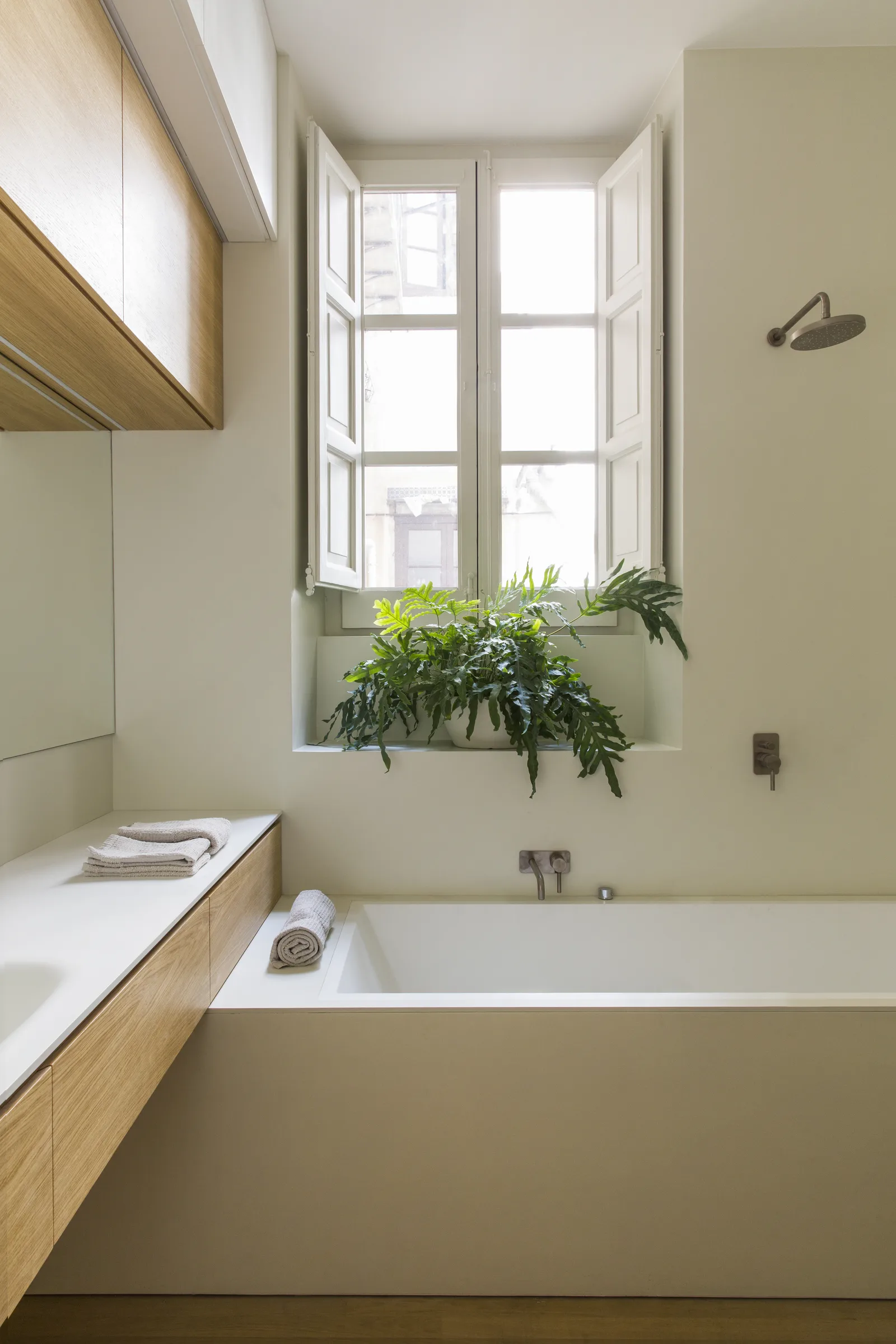 Bathroom with a rectangular bathtub, wooden cabinets and plants on the windowsill