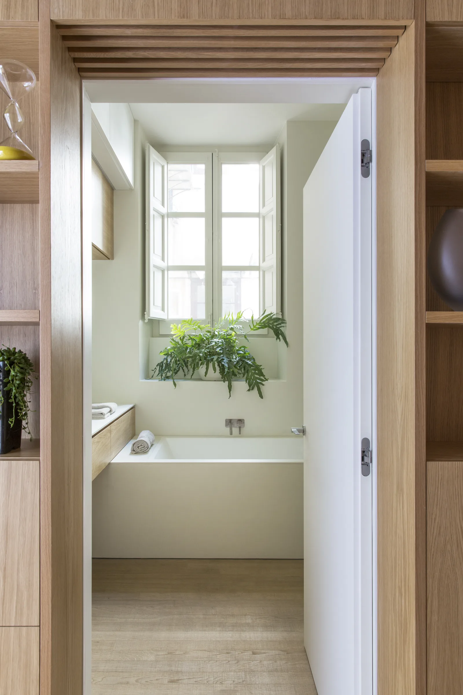 The bathroom seen through an oak-framed door, with the window and plants beyond