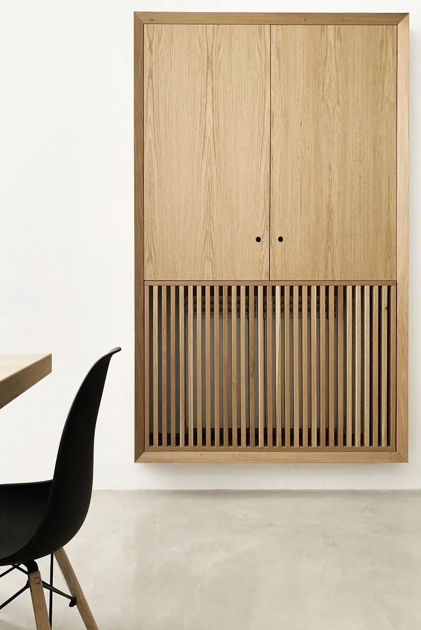 Wall-hung oak cabinet with a vertical-slatted lower part, beside a black chair