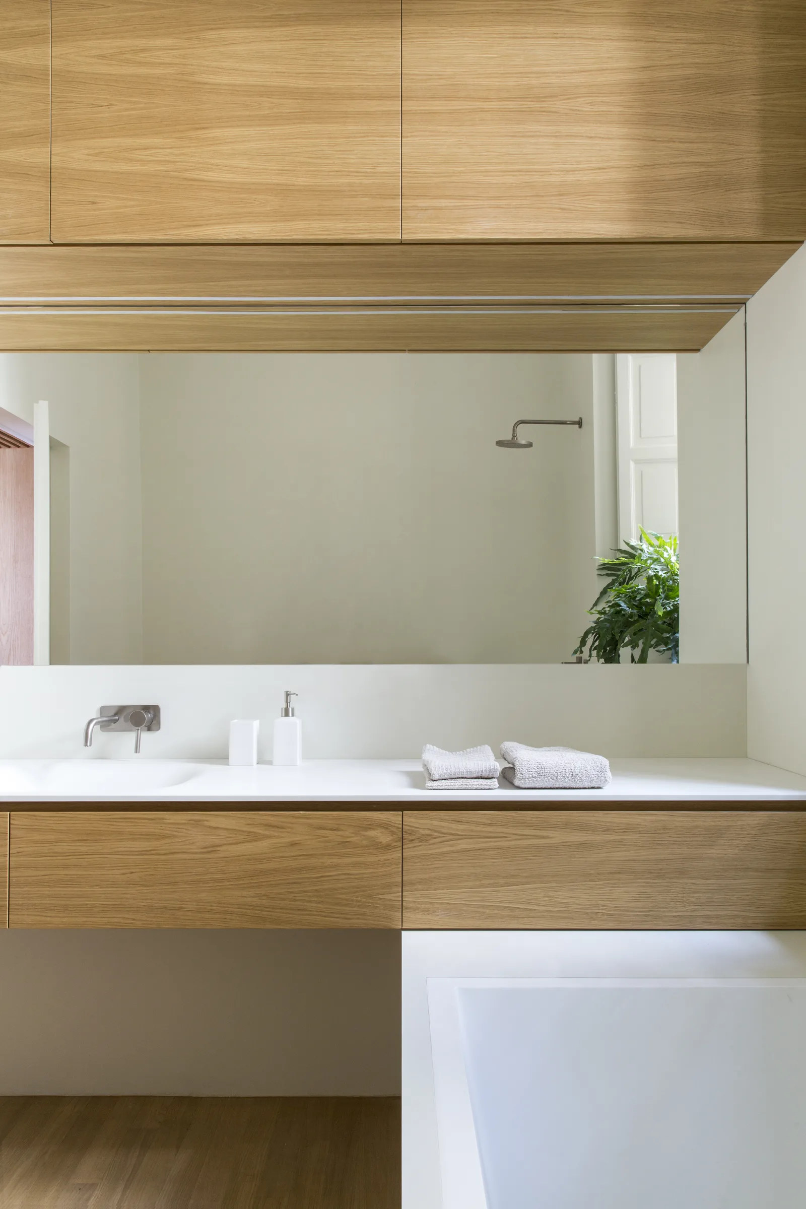 Wooden floating vanity with a large mirror and an oak wall unit