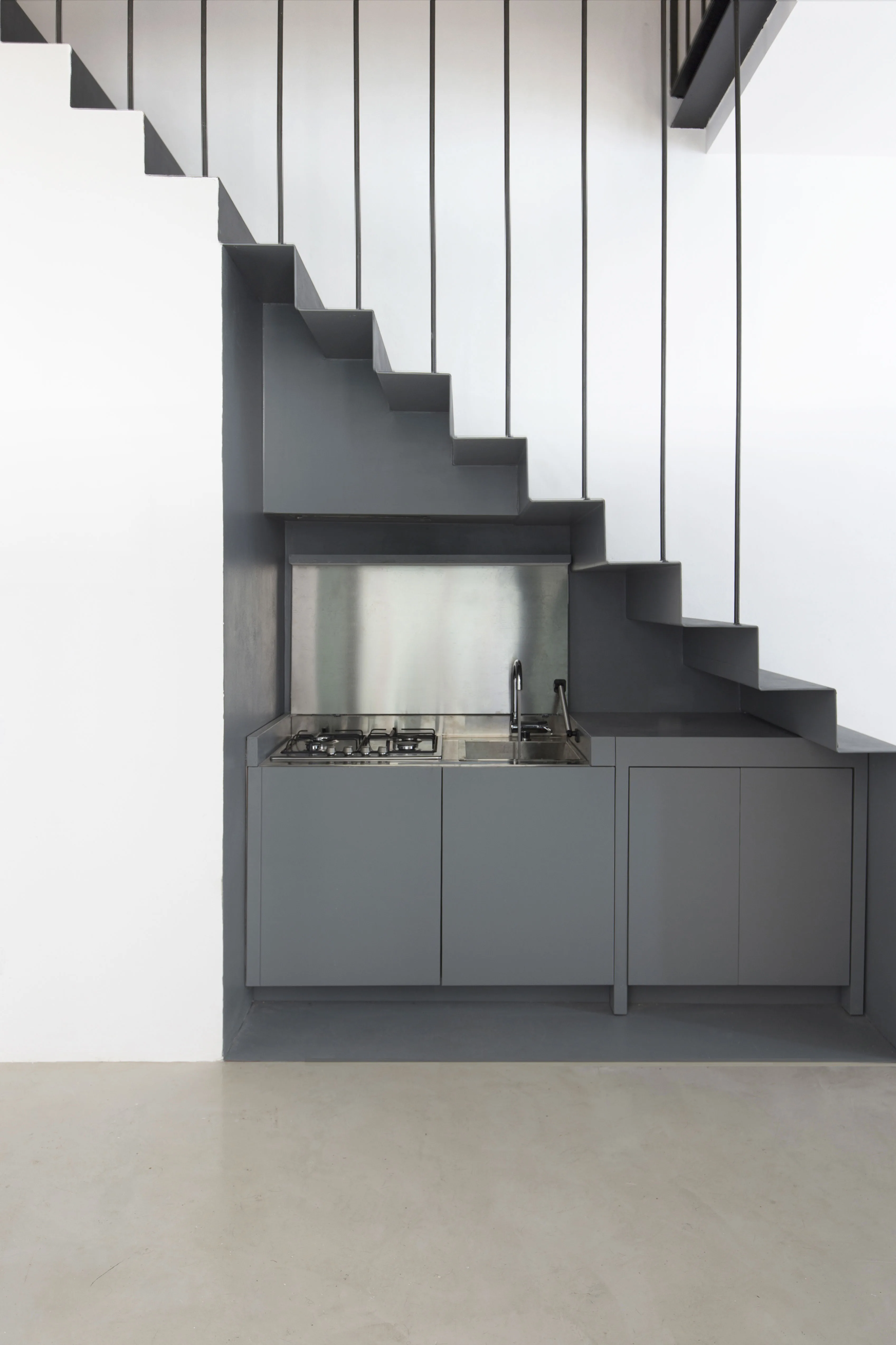 The grey kitchen under the stair, with hob and sink, on a pale resin floor
