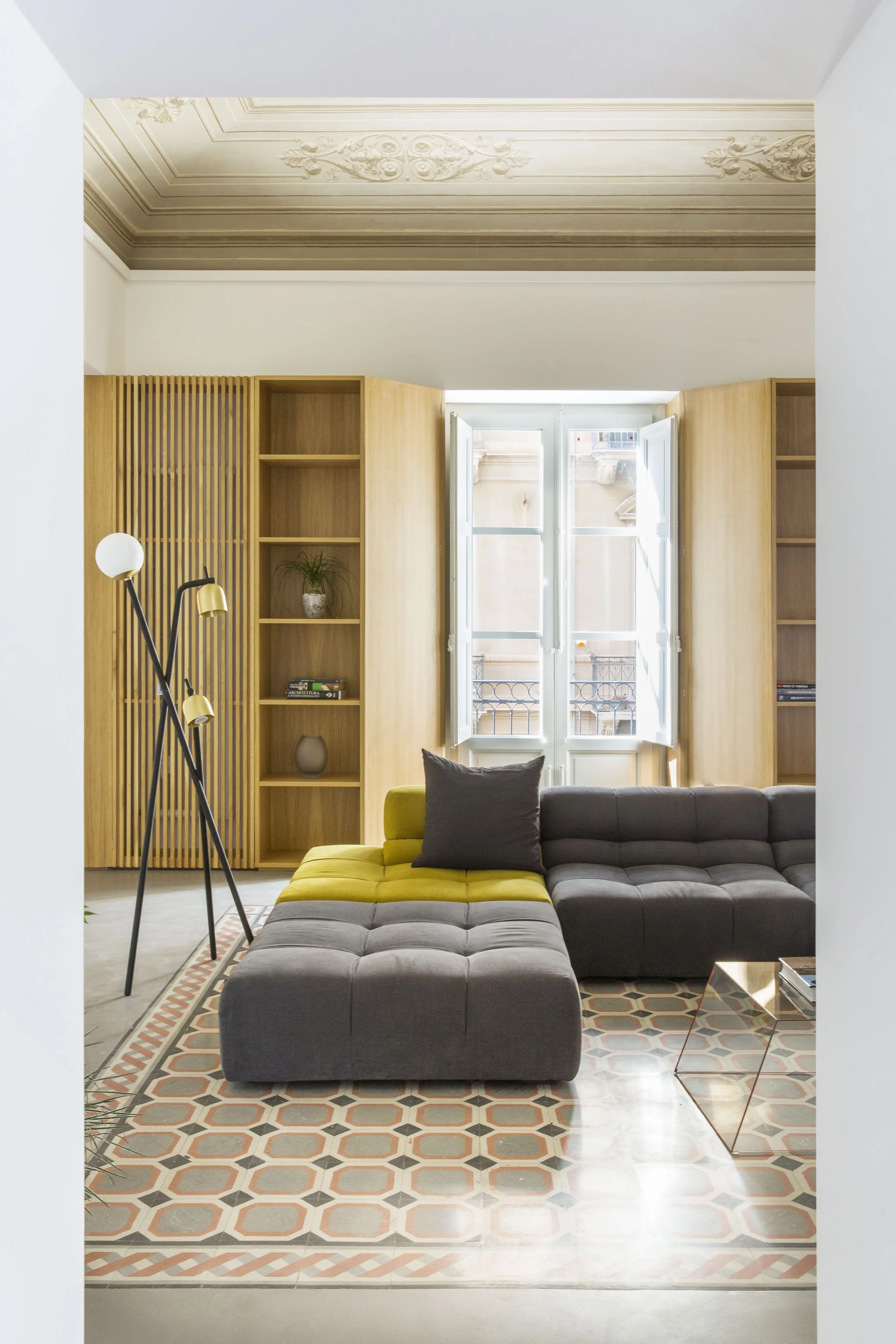 Grey sofa with a yellow cushion on a patterned tile floor, in front of the window
