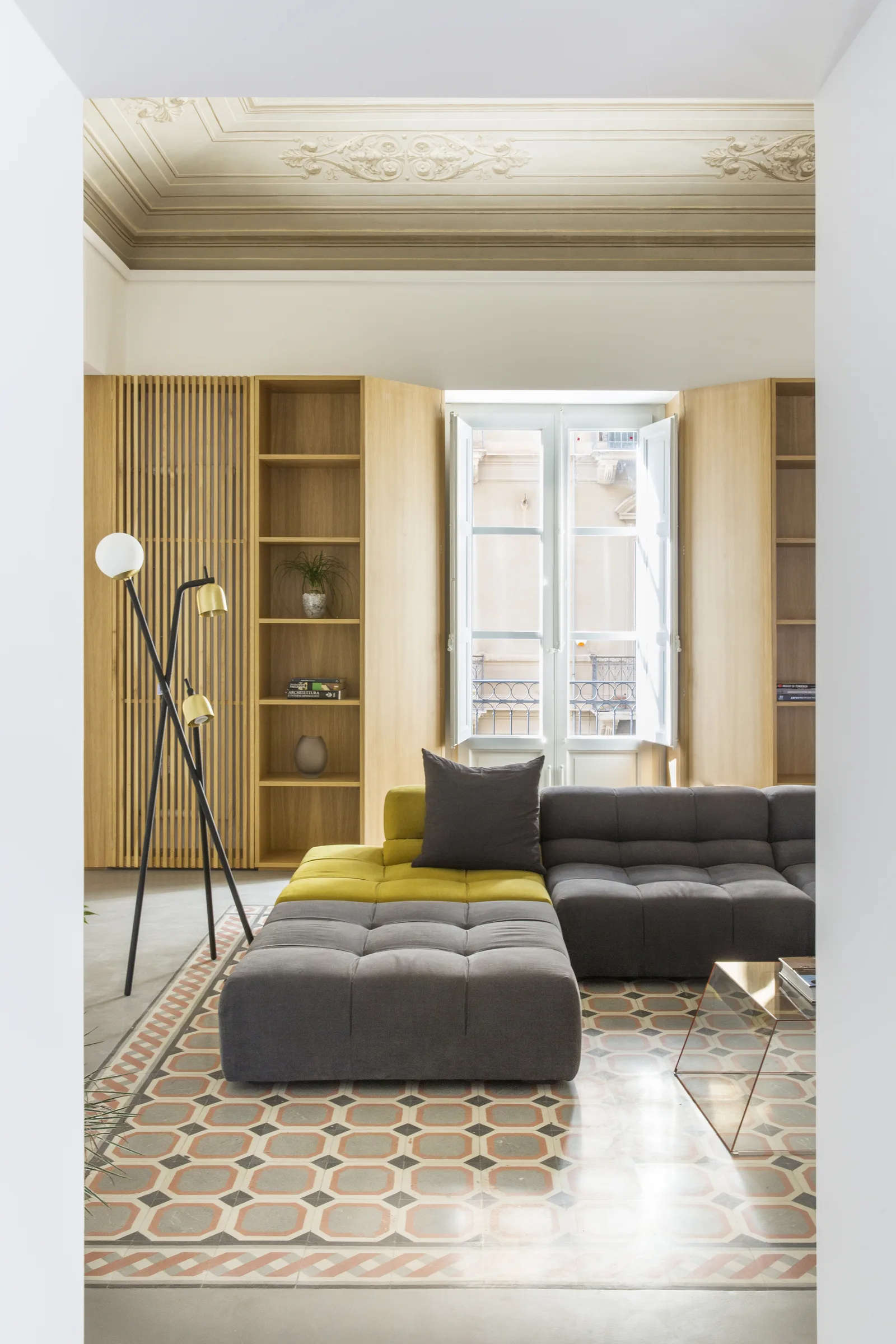 Grey modular sofa with a floor lamp in front of the bookcase and window