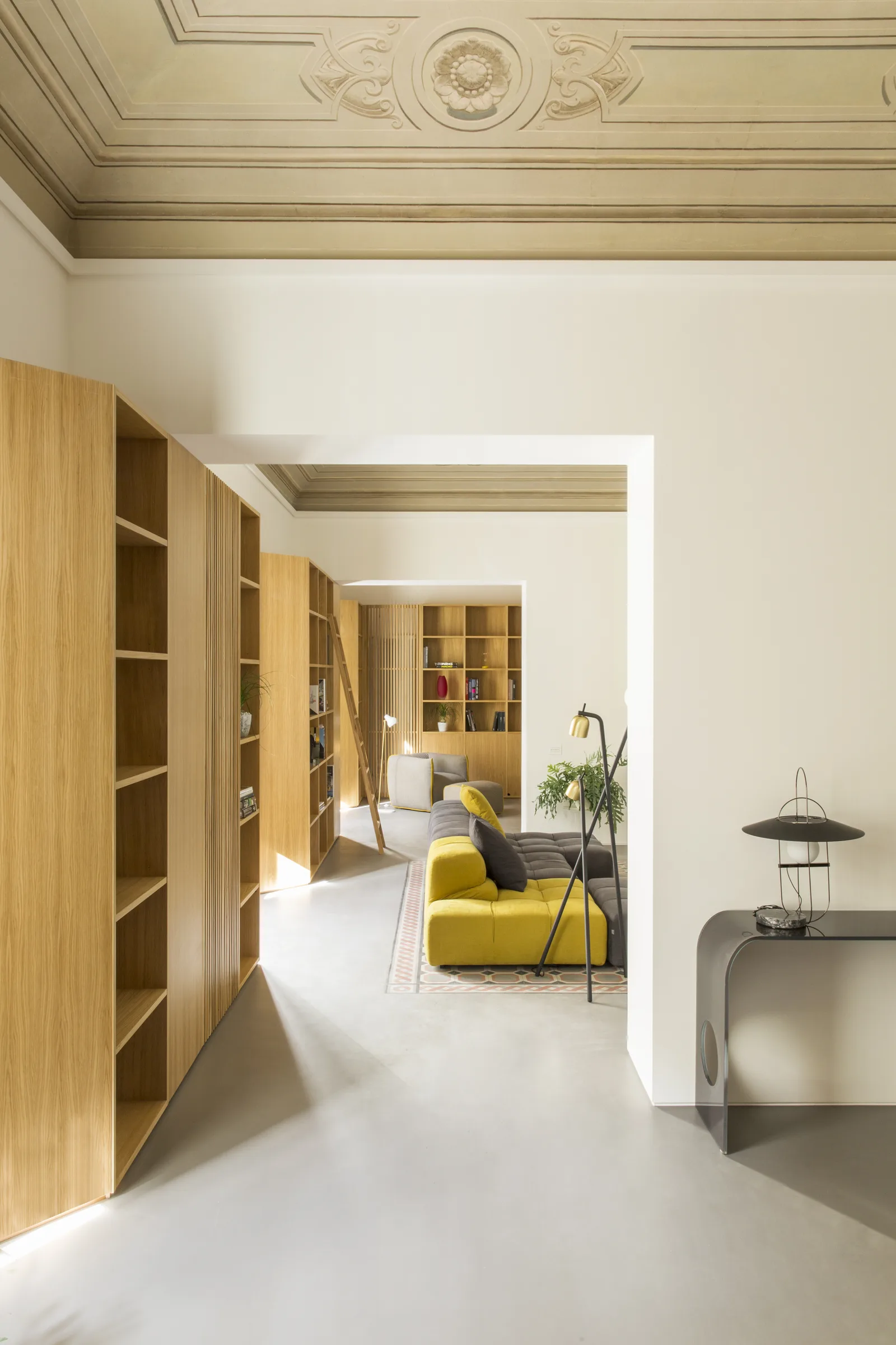 Corridor between oak bookcases towards a yellow sofa and a console table