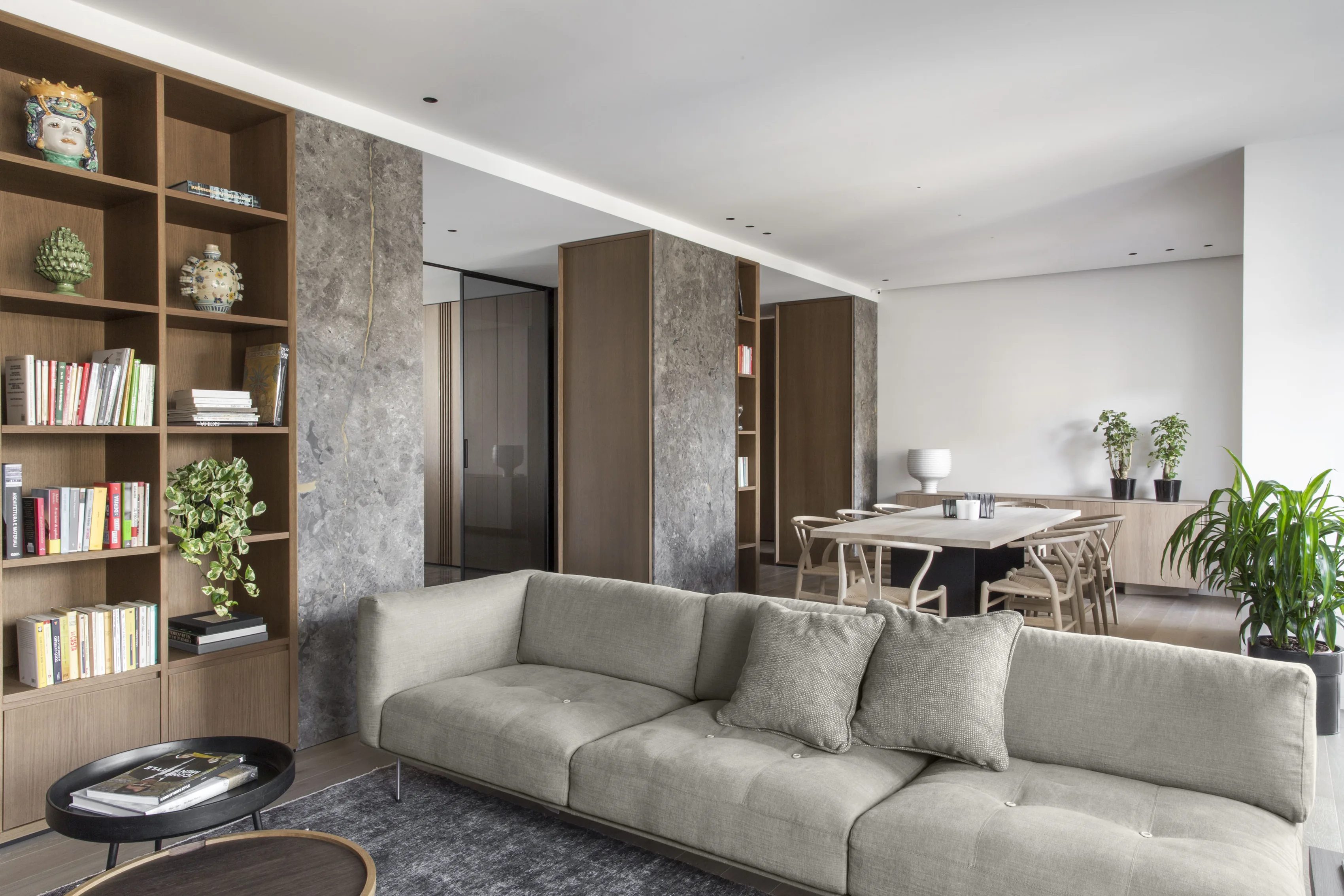 Living room with oak bookcase, grey stone pillar and pale sofa, with the dining area beyond