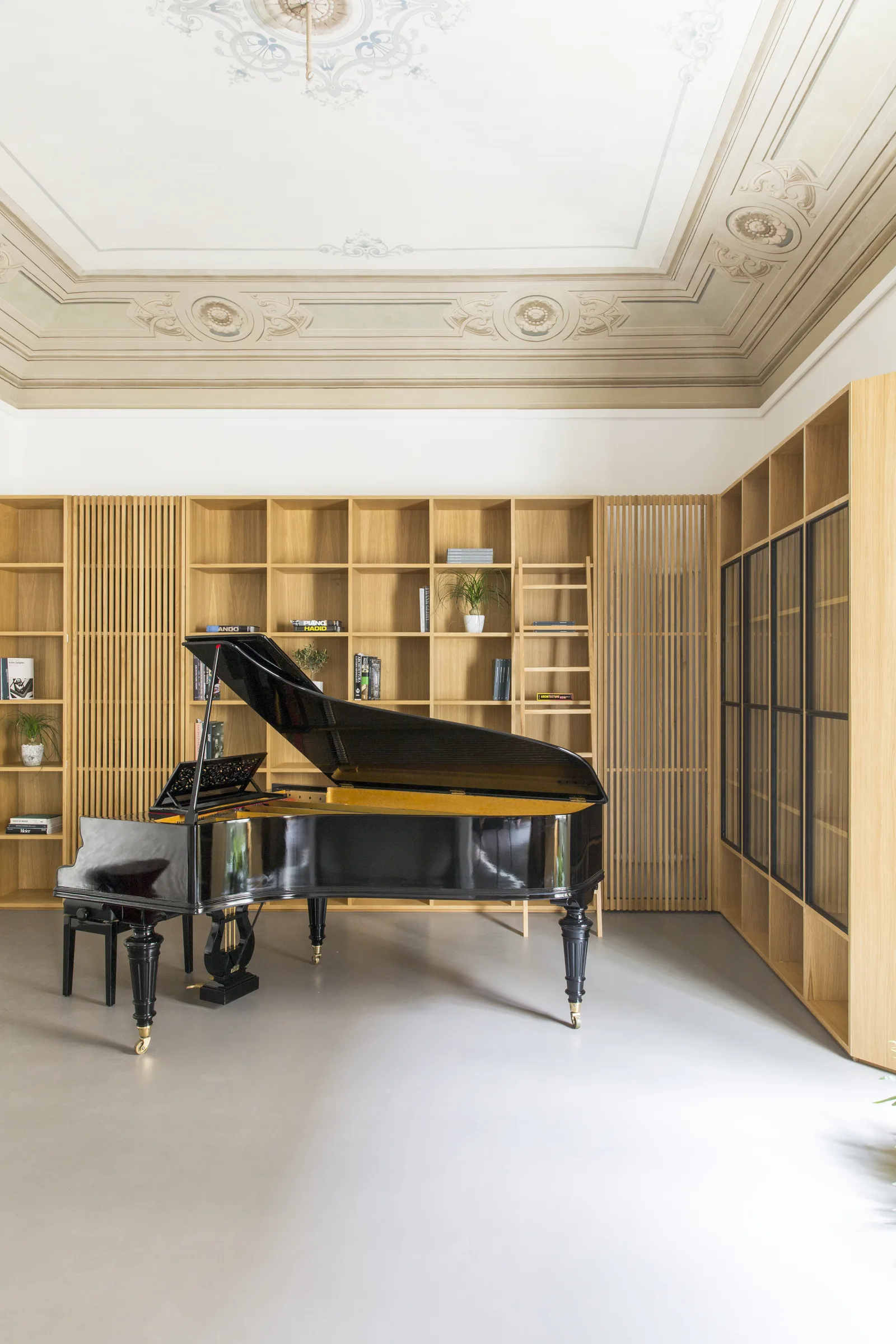 Grand piano at the centre of the room, between oak bookcases and glazed cabinets