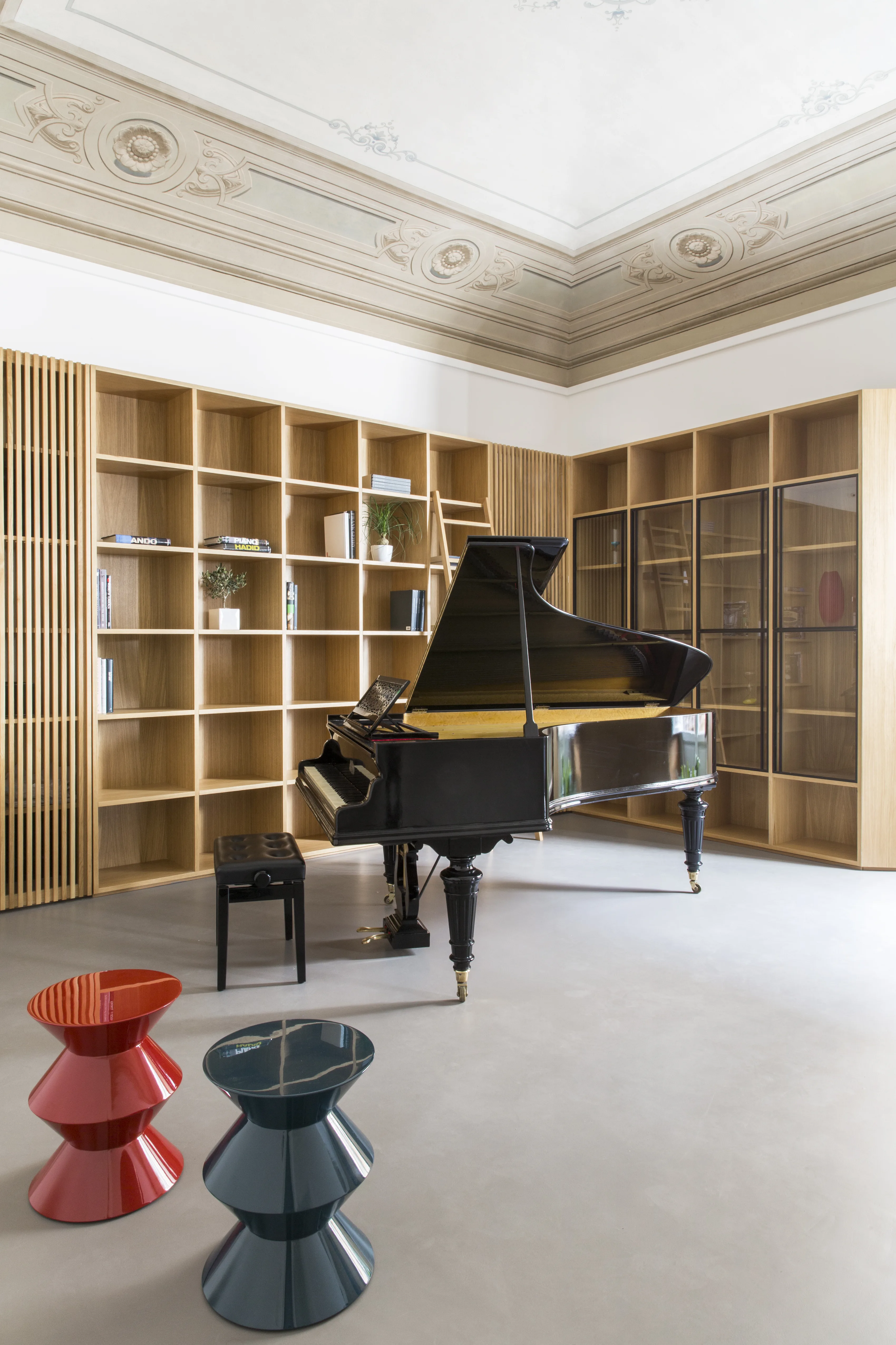 Music room with a grand piano, floor-to-ceiling oak bookcases and two colourful stools
