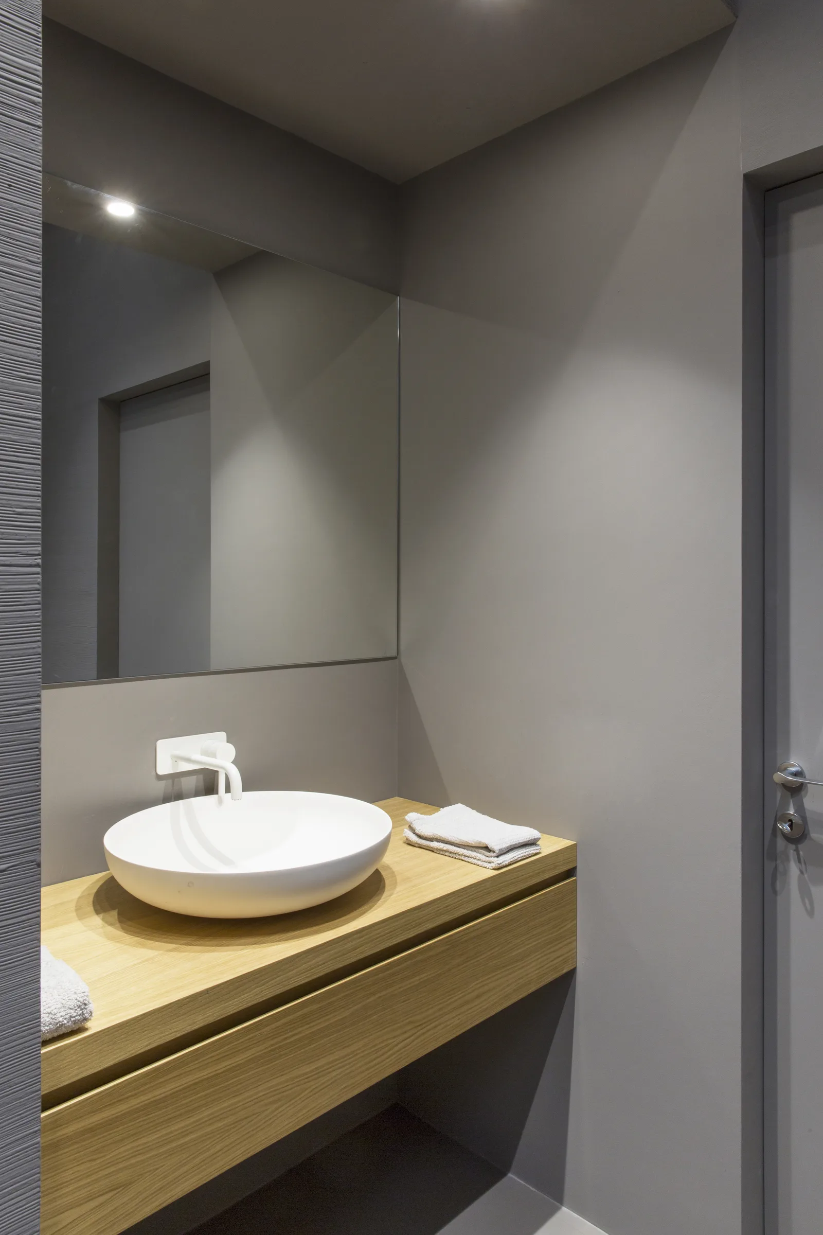 White vessel basin on a wooden top, with mirror and ceiling spotlight