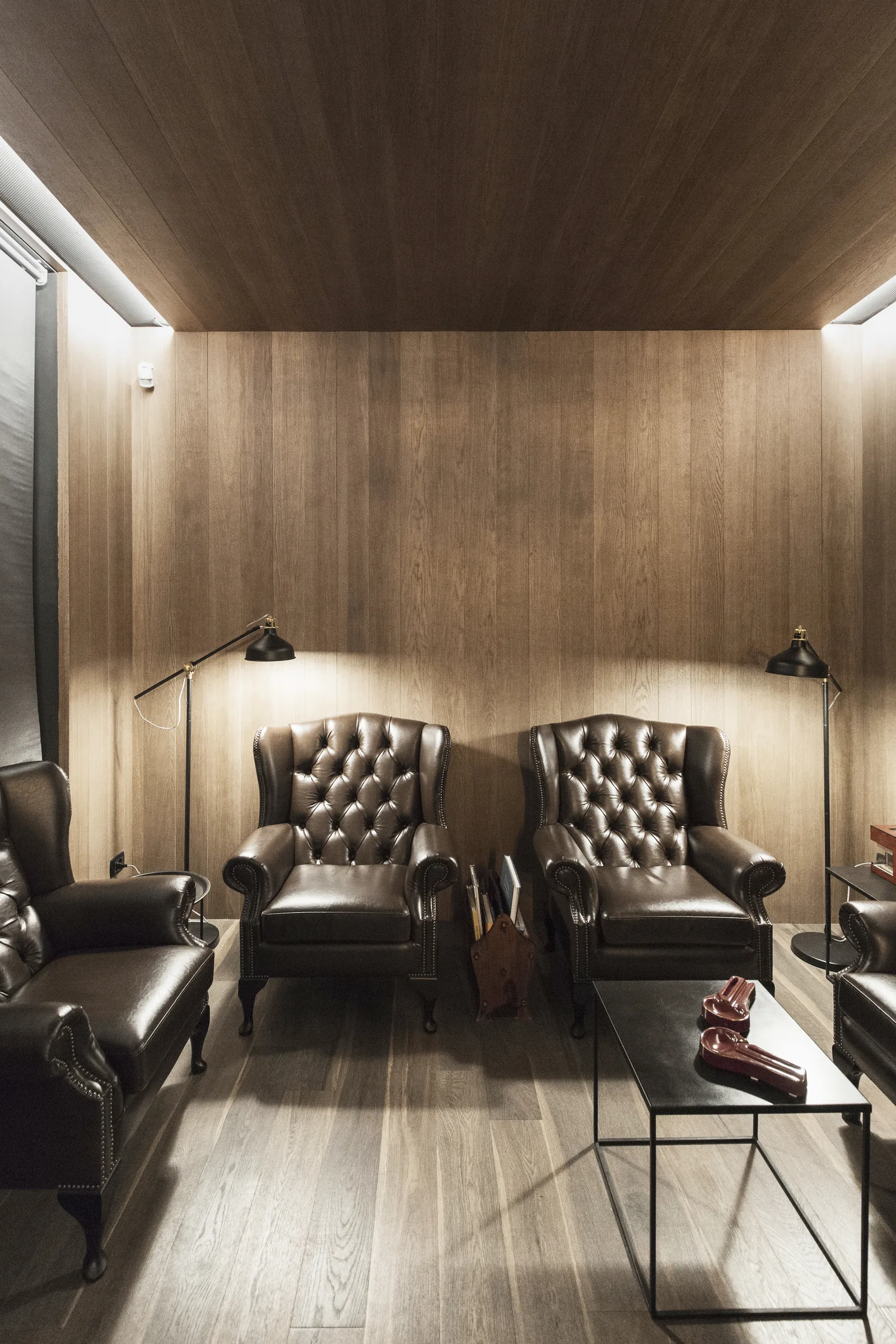 Saletta rivestita in legno scuro con poltrone Chesterfield e tavolino in metallo