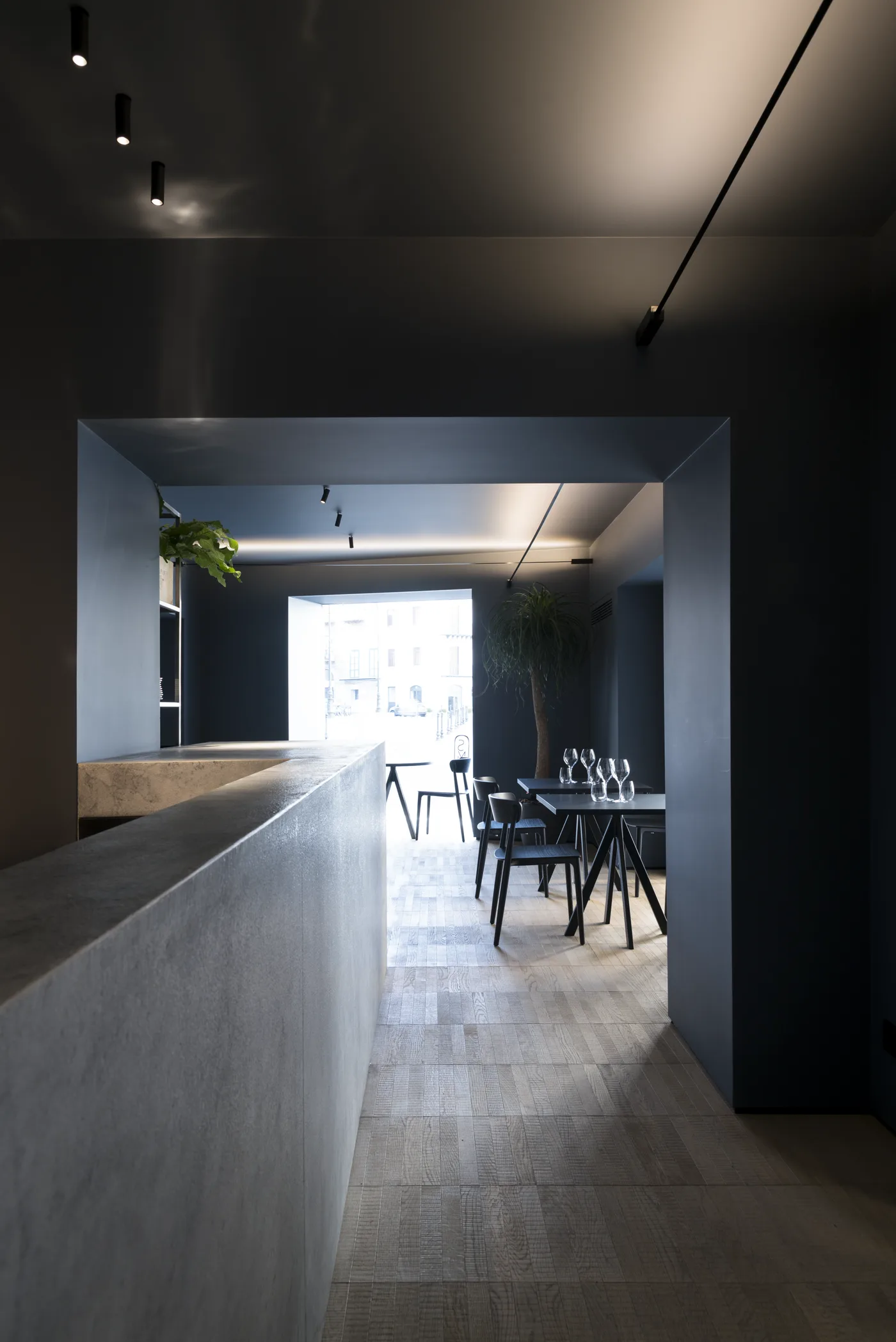 Sala lunga vista lungo il bancone in pietra chiara, con tavoli in fondo e la luce della finestra