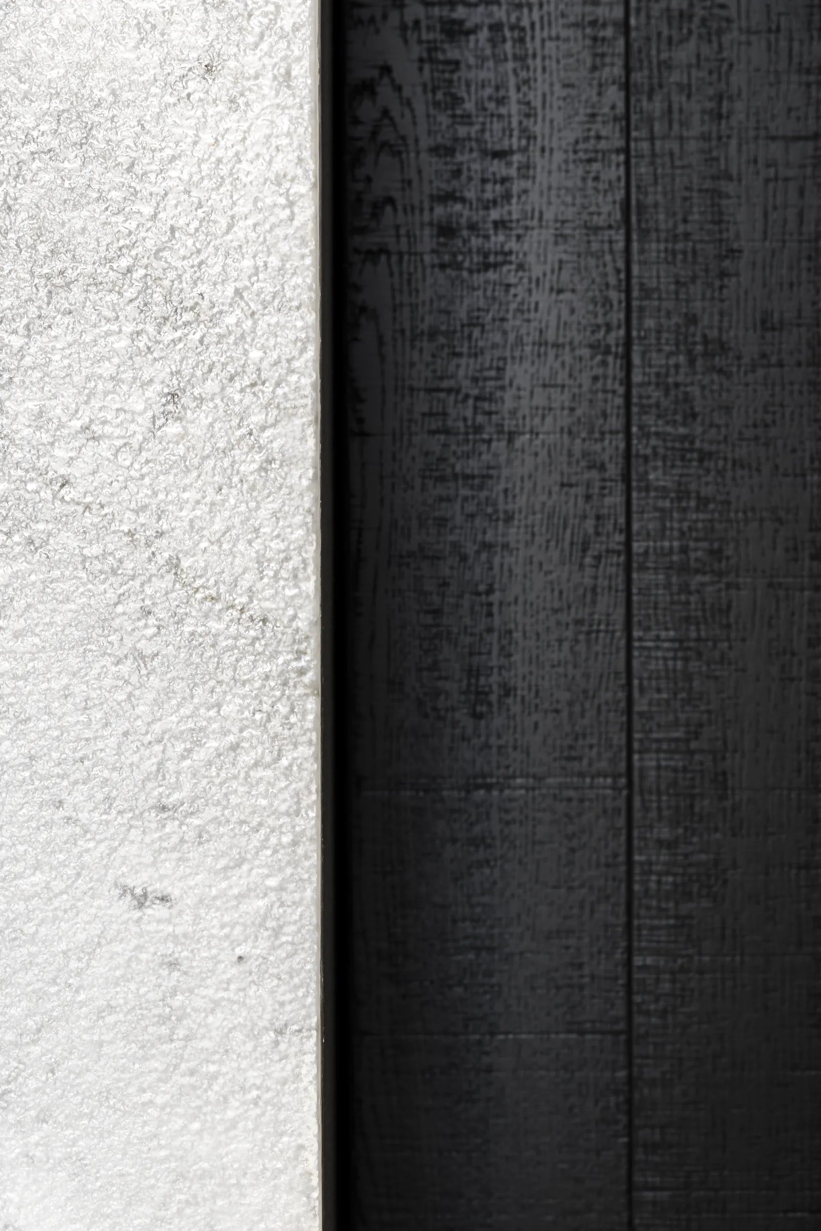 Giunto verticale tra il muro intonacato chiaro e le tavole in legno nero