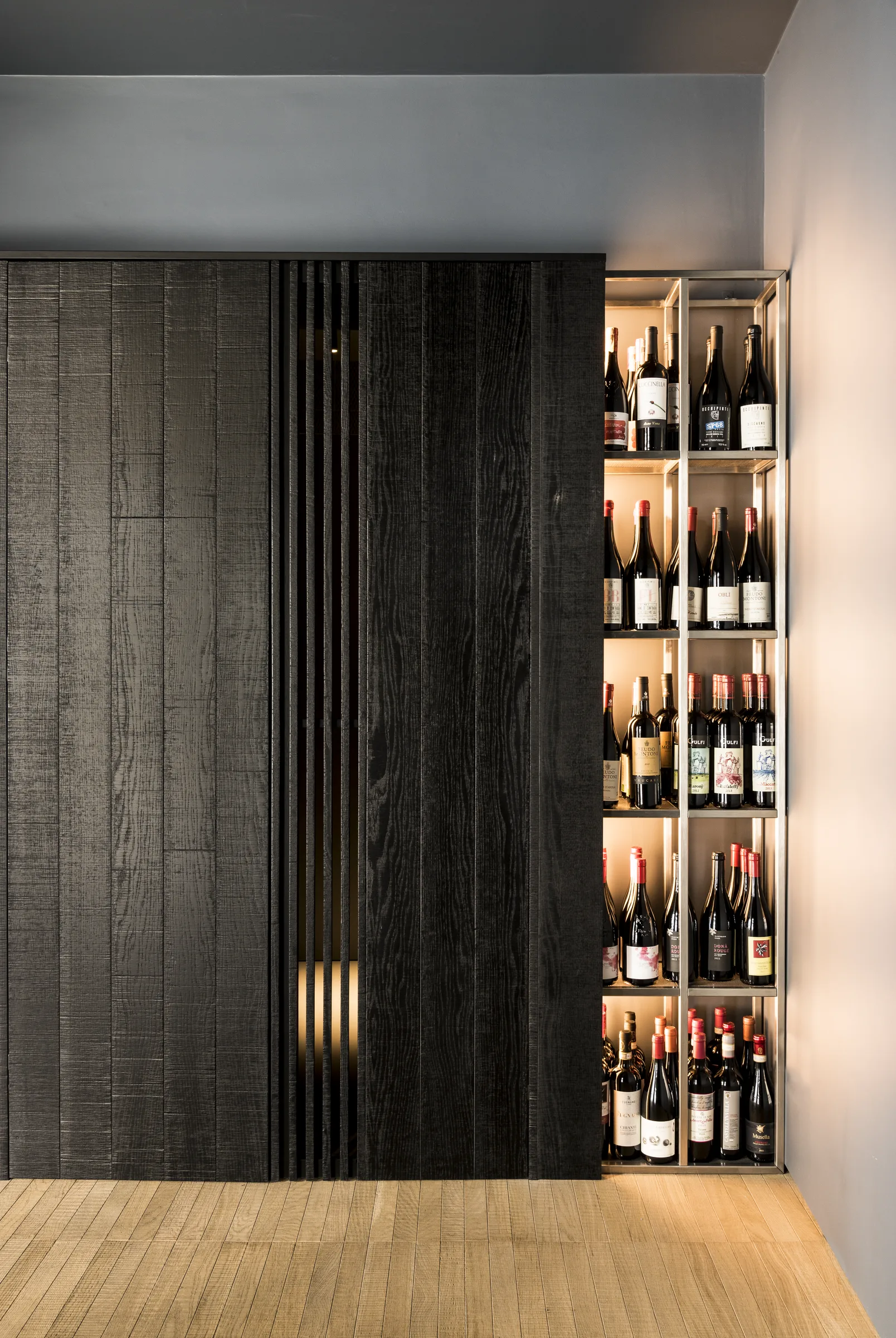 La stessa parete di legno con la vetrina di vini e la luce calda sul pavimento, in verticale
