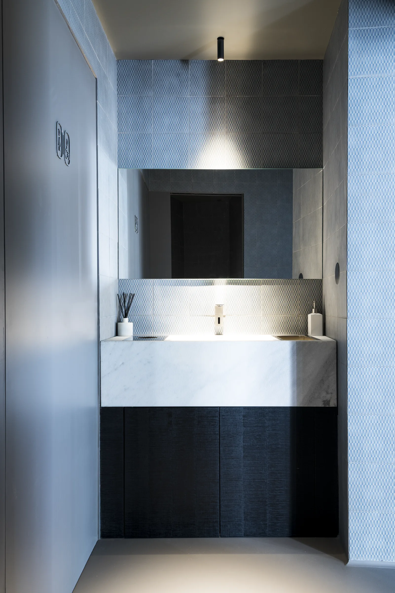 Lavabo in pietra chiara con specchio e rubinetto metallico, sopra un mobile scuro, nel bagno azzurro