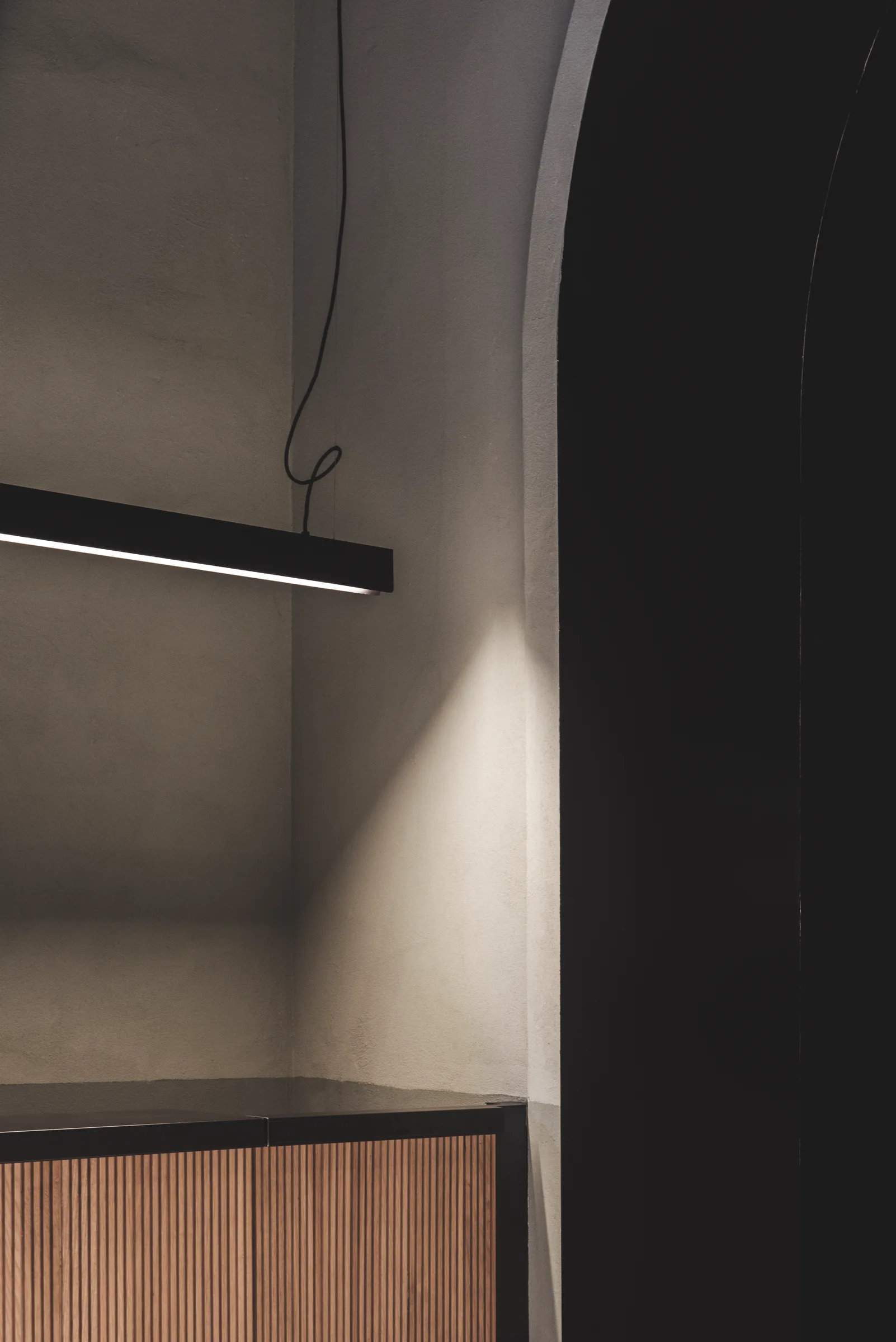 Nicchia con lampada lineare a sospensione sopra un piano in listelli di legno e nero