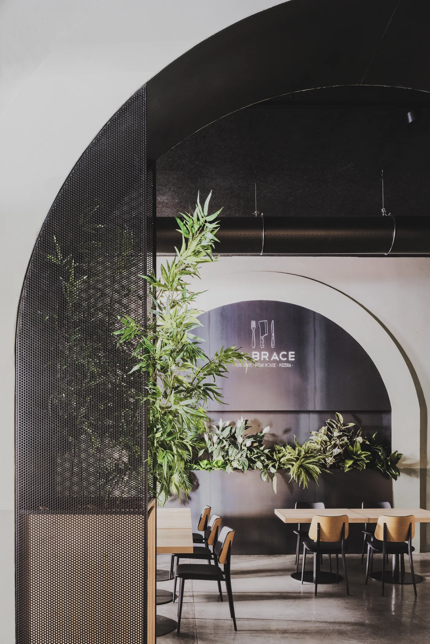 Sala con grande arco in intonaco chiaro, pannello forato nero, piante e tavolo lungo sul fondo