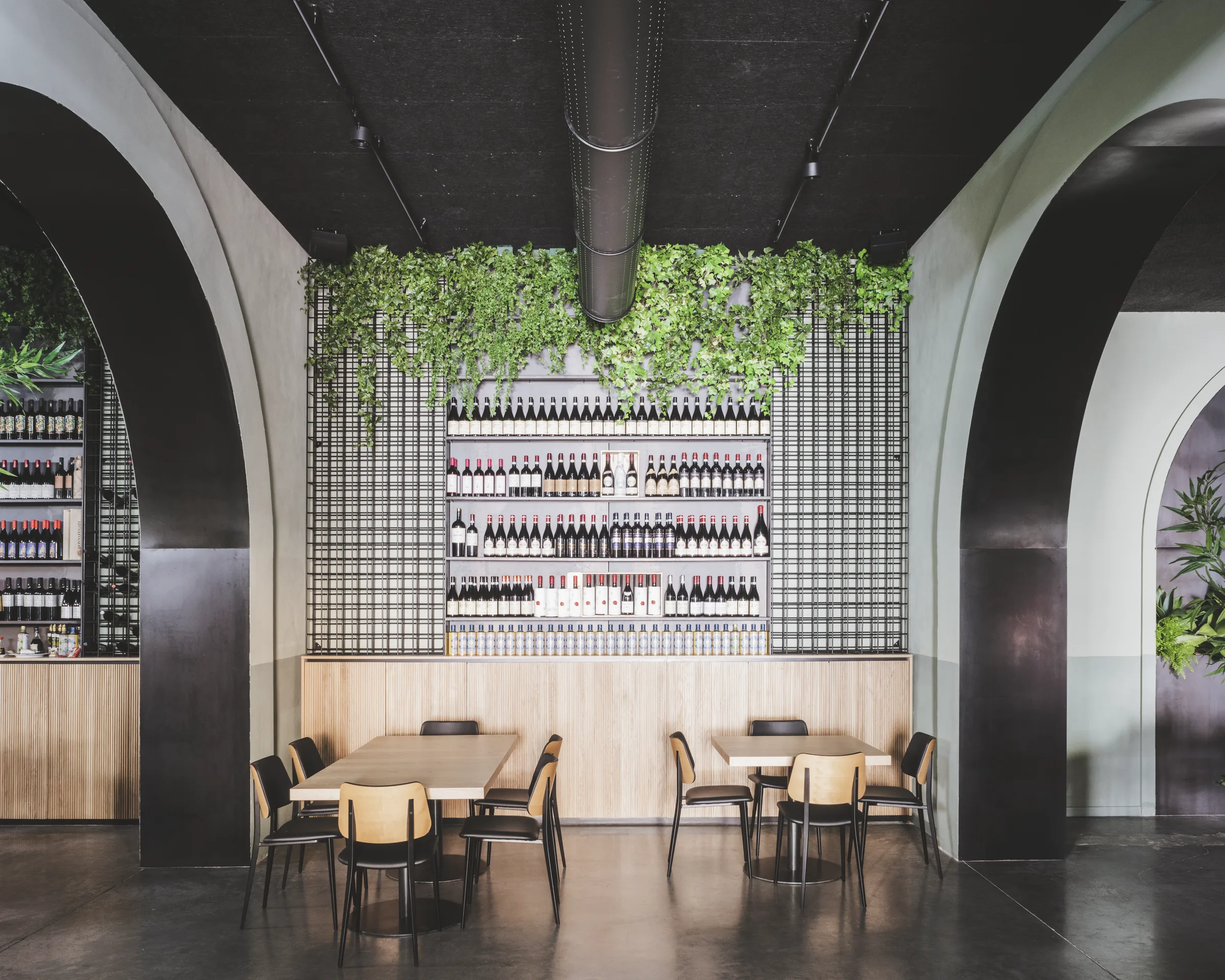 Sala col tavolo comune e la cantina a vista con vini, griglia metallica e piante pendenti